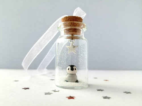 Miniature penguin decoration. Little pottery penguin chick in a glass bottle. Christmas mini penguin ornament