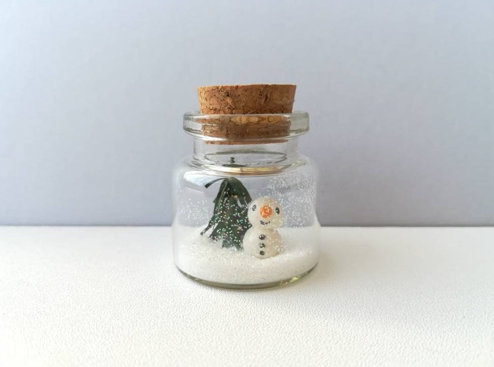 Miniature snowman Christmas decoration. Little pottery snowman and tree in a glass bottle. Christmas mini ornament