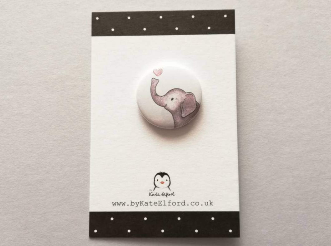 Mini round white button badge, it has an illustration of a grey elephant with a pink heart above it's trunk