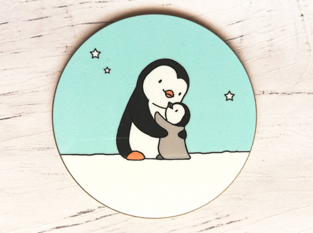 Penguin coaster. A black and white penguin and a grey penguin chick in the snow hugging. There is a light blue sky with a few stars