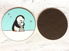 Load image into Gallery viewer, Back and front of a penguin coaster. A black and white penguin and a grey penguin chick in the snow hugging. There is a light blue sky with a few stars
