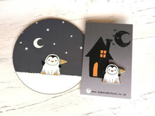 Load image into Gallery viewer, Round coaster. A little penguin dressed as a ghost. There are stars and the moon in the sky behind. Penguin is holding a flag that says Boo. Also pictured is a matching enamel pin
