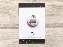 Load image into Gallery viewer, Mini button badge. A small round badge with a white background. The picture is a black and white penguin wearing a rainbow colour striped jumper
