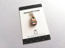 Load image into Gallery viewer, Small wooden stitch marker, little penguin design wearing a rainbow striped jumper. Eco friendly wood
